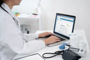 Médica escrevendo sobre histórico de paciente em prontuário eletrônico integrado em computador.